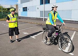 Photo of a cyclist riding a bike with an instructor standing nearby